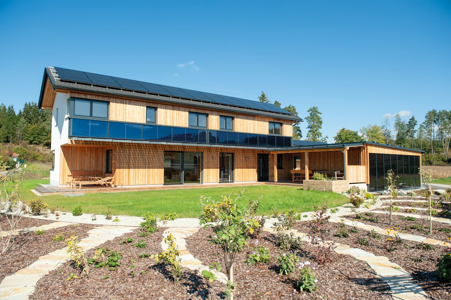 Modernes Haus mit Solaranlagen und einem angelegten Garten.