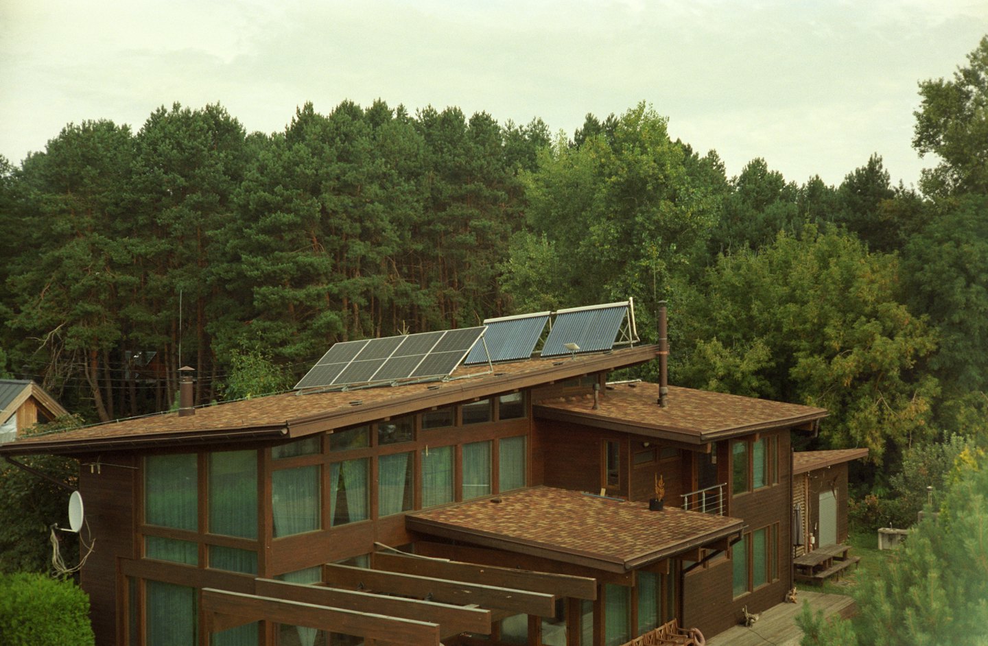 Modernes Holzhaus mit Solaranlagen auf einem waldgedeckten Dach.